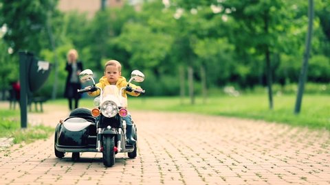 Happy little boy driving a toy motorcycle in a park