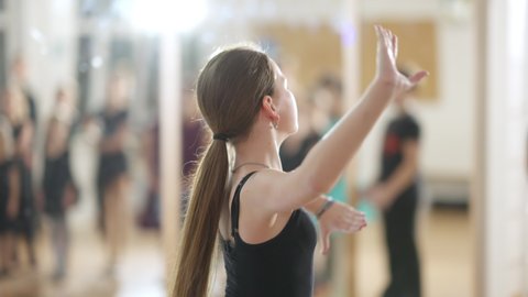 Camera follows slim Caucasian girl waltzing in fourth position with group of blurred children watching. Talented child showing ballet movement to classmates in dancing school. Skill and art.