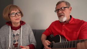 Lovley married couple of retirees sing a song while sitting at home on the couch. A man plays an acoustic guitar. Happy couple - Powered by Shutterstock - Get 15% off with code: PIKWIZARD15
