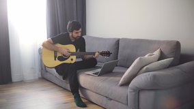 A young man plays the guitar through a video call on a laptop.
