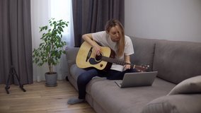 A young woman plays the guitar through a video call on a laptop.