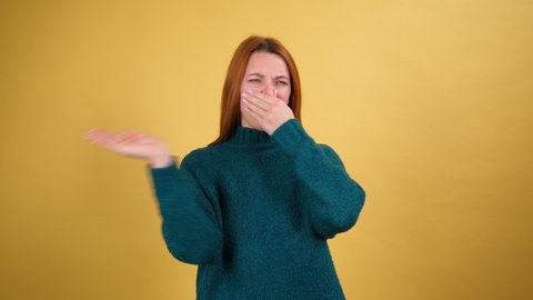 Repulsion to bad smell. Ginger hair girl grabbing nose with fingers, holding breath to avoid stink, awful fart gases, intolerable odor, showing stop gesture. Studio shot isolated on yellow background