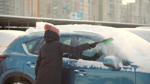 Sweep Snow From Automobile With Brushes In Winter.Scraping Ice From Glass.Woman Cleaning Car After Snowfall.Brushing Snow And Ice From Car Glass.Female Cleaning Fresh Snow After Snowstorm From Vehicle