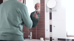 Elderly man brushing his teeth and looking himself in the mirror in bathroom - Powered by Shutterstock - Get 15% off with code: PIKWIZARD15