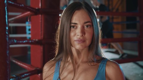 Lviv, Ukraine - 20 September, 2020: Attractive caucasian girl wearing black boxing goves punching at camera having fun during training in gym club. Professional boxing ring. Athletic lifestyle.