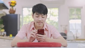 Asian high school boy is playing online game on his mobile phone at home.