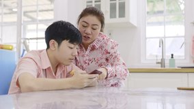 Asian high school boy with his mother are playing online game on his mobile phone at home.