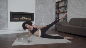 young multiracial woman doing her exercises at home using a laptop to repeat moves from video classes