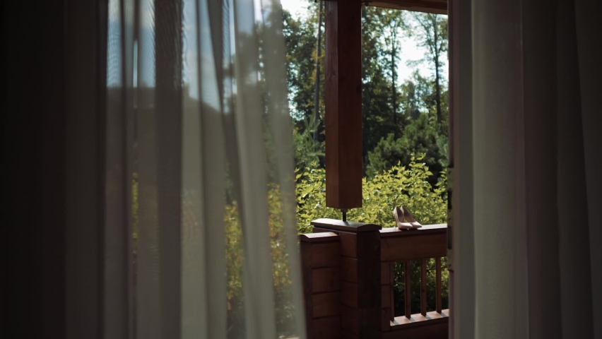 View from the house to the veranda through the open door. There are shoes on the porch railing. Wedding frame. High quality FullHD footage