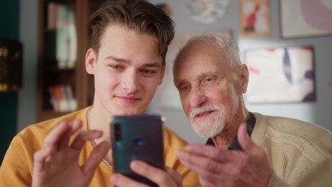 Grandfather and grandson using phone, young student teaching grandparent how to use smartphone applications, watching funny video, playing game, looking at cellphone screen