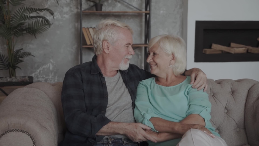 Grey haired couple in love embracing sitting on couch smiling looking at camera feels healthy, harmony in relationships, happy long life together, anniversary, older people services insurance concept Royalty-Free Stock Footage #1067759198