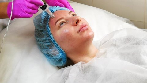 Dermapen skin treatment. Professional cosmetologist is doing procedure of fractional mesotherapy for young woman. Micro needling against acne, wrinkles and large pores. Hardware cosmetology in clinic.