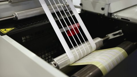Close-up video of label manufacturing on flexo printing machine. Detail of matrix waste or trim removal from adhesive material on flexographic press in the printing industry.