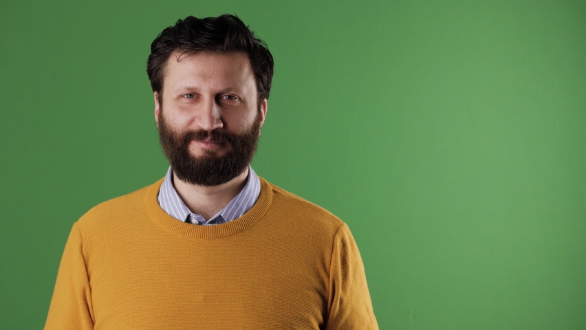 Man holding number 74 sign. Cheerful white bearded good-looking man in yellow sweater shows number seventy-four on white sheet. Chrome key, green screen, copy space
