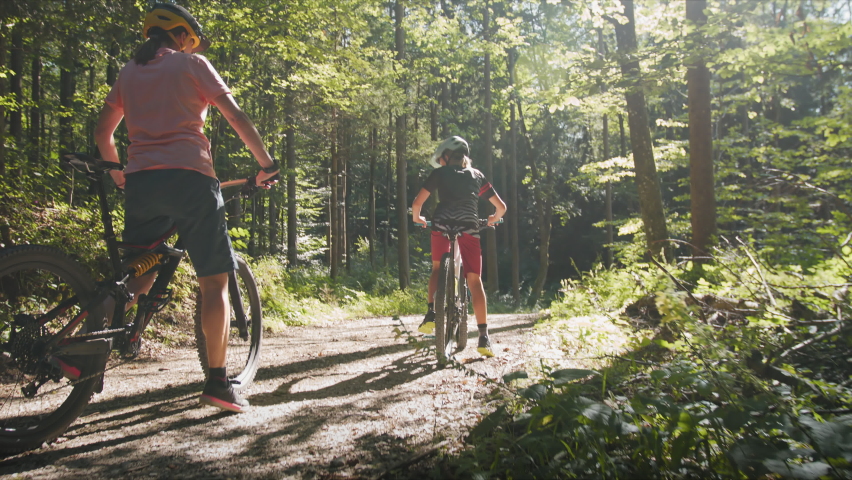 Two girls on mtb bikes. Mother and daughter riding on a forest trail with sunshine.