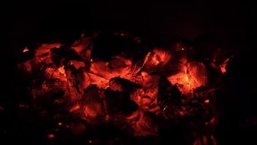 4k resolution video with burning hot wood coal on the fire pit in the darkness. Glowing warm red and romantic dark background without flames. Outdoor fireplace with copy space