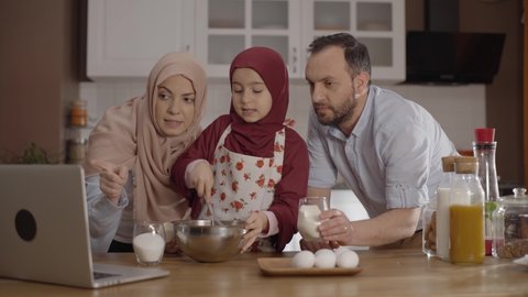 The Muslim family and their little daughter watch the recipe on the computer and cook together. Recipe online. Family cooking, having fun together, spending time concept.