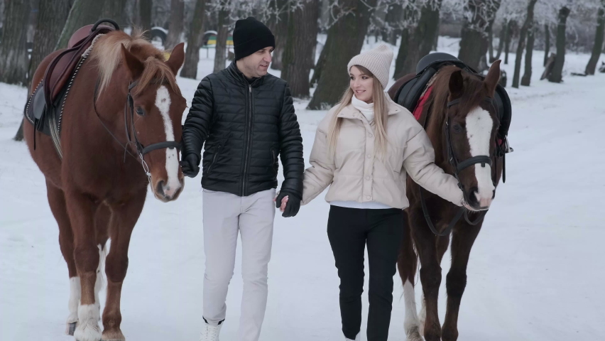 Couple in love with horses in winter forest 4K. Romantic walk