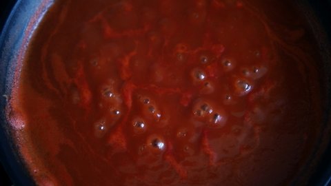 Close-up macro detail overhead view of bubbling hot red fresh tomato sauce for pasta or pizza boiling in stove pan on kitchen. Homemade cooking background