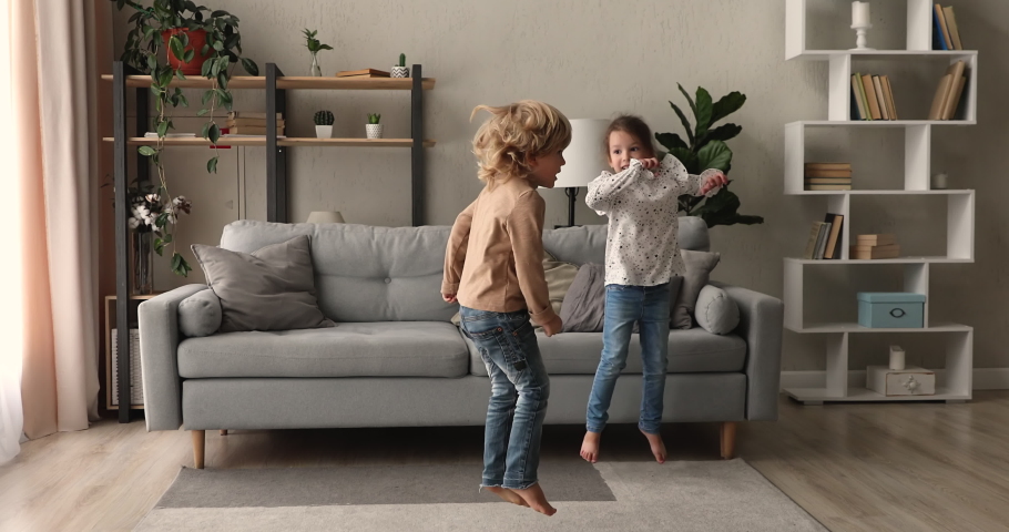 Happy two adorable energetic little preschool kids siblings having fun, jumping barefoot or dancing to disco music in living room, enjoying playful domestic childish activity together indoors. Royalty-Free Stock Footage #1067779271