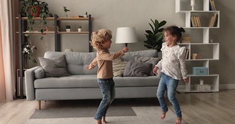 Happy two adorable energetic little preschool kids siblings having fun, jumping barefoot or dancing to disco music in living room, enjoying playful domestic childish activity together indoors.