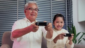 Little girl playing video game with her grandfather at home. They playing with funny emotion together.