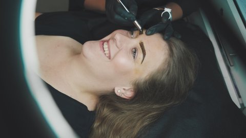 Close-up process of permanent makeup of eyebrow . Master in gloves, using special needle, injects pigment into the skin and stains the eyebrows using hair technique, making them natural.