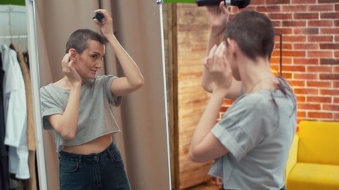 A woman shaves hair with a hair machine. Woman at the mirror changes style and is happy with the new haircut