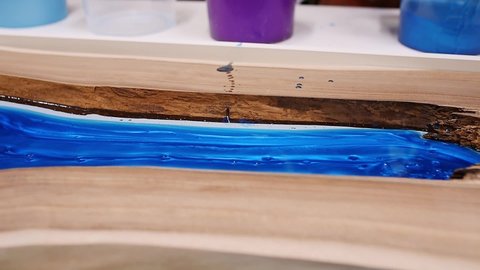 Process making of a craft resin and wood table. Liquid epoxy is poured into a mold with wooden blanks.
