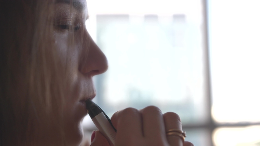 the girl smokes the vape blows smoke from her mouth in slow motion