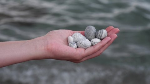 Defocused sea round beautiful gray stones lie in a female hand against background of sea and water. Concept of rest, vacation, relaxation, spa, meditation. Stones in hand. Screensaver for relaxation.
