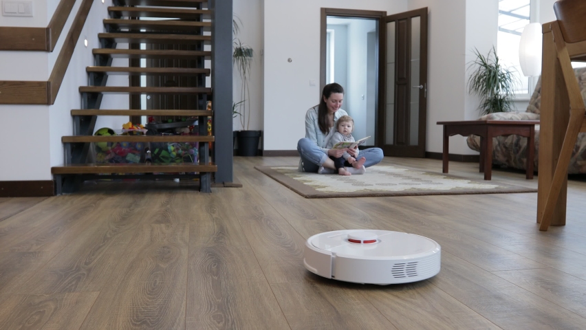Robot vacuum cleaner cleaning in a living room while mother and a child playing indoors. Automatic vacuum cleaner  | Shutterstock HD Video #1067800139