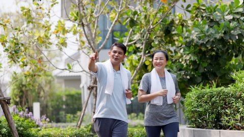 Happy family Asian elderly couple jogging in the village garden. Senior man and woman do morning workout For good health. Park with nature for relaxation. Concept Health insurance