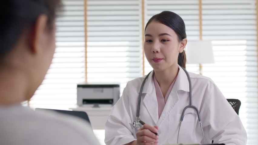 Attractive beautiful young asia doctor female wear white gown stethoscope on shoulders diagnosis talk to sick patient provide help counseling consult, therapy or explain prescribe in office clinic. Royalty-Free Stock Footage #1067806688