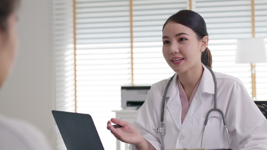 Attractive beautiful young asia doctor female wear white gown stethoscope on shoulders diagnosis talk to sick patient provide help counseling consult, therapy or explain prescribe in office clinic. | Shutterstock HD Video #1067806688