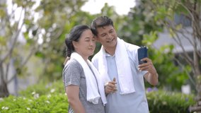 couple asian senior man and woman feeling fresh and using smartphone to selfie or video call. Close up portrait of people after walking and exercise at garden. Healthy lifestyle for older people.