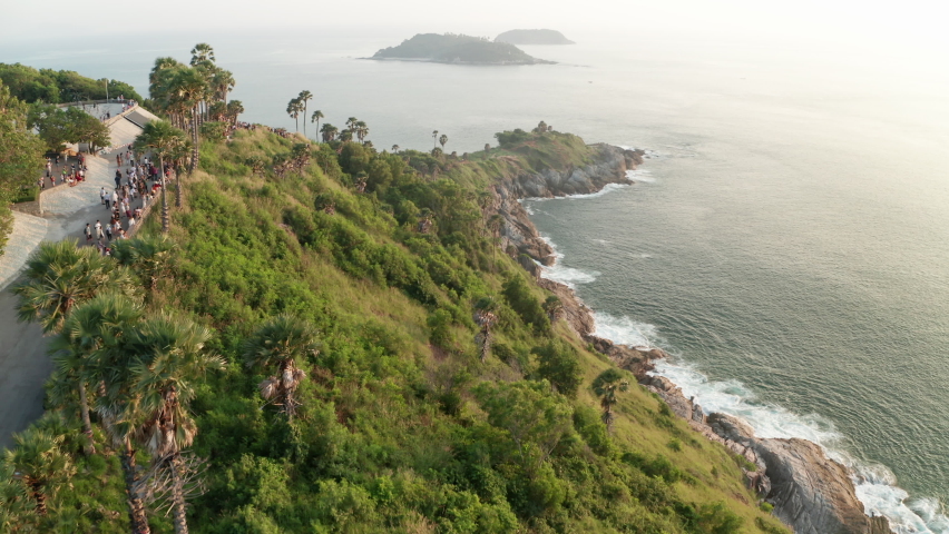 Aerial tracking shot of a beautiful lagoon by the side of the ocea, filled with tropical trees and lush plants, white foam of waves crashing against the rocky foot of the cliff