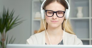 Young smiling woman in headphones talking on a video call online. Happy girl greeting waves waving in webinar remotely using laptop. Student learns looking at webcam while at home.