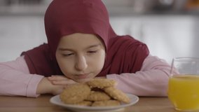 The little Muslim girl wearing a hijab eagerly looks at the cookies.Slow motion video.