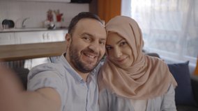 Bearded young man with his wearing hijab muslim wife taking a victory sign selfie. Front camera view.