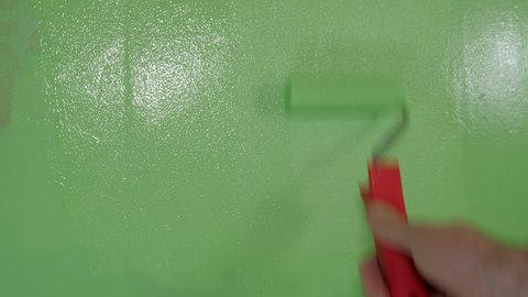 A small red rollers painting the wall during the home repair with the green paint