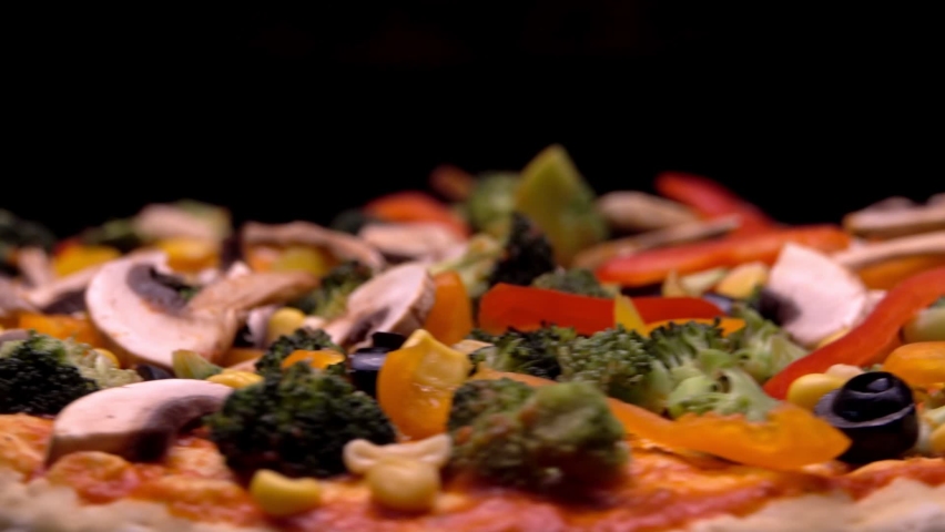 Raw Pizza with fresh vegetables. Cine Camera rotation around the pizza with fresh broccoli, olives, mushrooms, Bulgarian colorful peppers. Meal isolated on black background. 4K cine camera close up