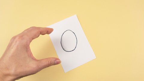 4k Drawing of an egg appears on a white piece of paper. Then the Woman's hand takes out real chicken egg from drawn one. Yellow background. Easter creative concept. Copy space. Stop motion animation.