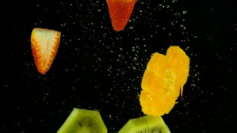 kiwi, strawberry, orange splashing into water on black background. Falling fresh fruits and berries in water. Organic berry, healthy food, slow motion.