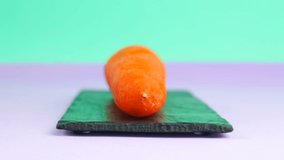 Stop motion animation a large orange carrot is cut and reassembled. Cartoon healthy vegetarian food concept. Chopping carrot close up on slate stone black board.