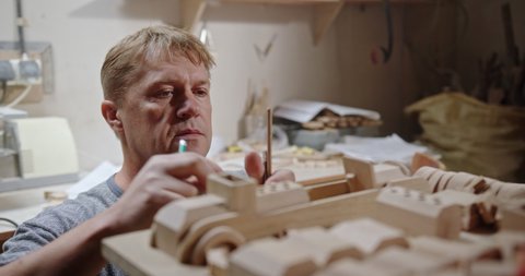 Craftsman constructing wooden toy in carpentry studio. Skilled middle aged carpenter putting pencils into drilled holes in wooden detail while assembling toy vehicle in workshop