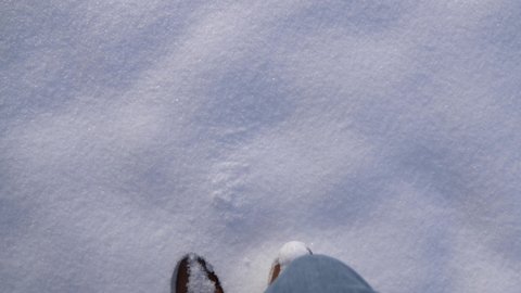 POV close up of boots walking through thick fresh powdery snow in slow motion on a sunny winter day in Bavaria, Germany.