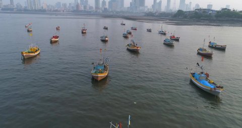 Flying over the fishermen's boats parked at the Koliwada next to Worli Fort, revealing the Mumbai Cityscape view of skyscrapers in the back with settlements to contrast.