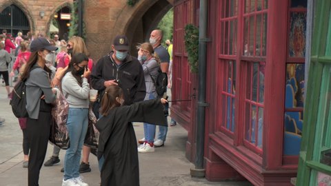Orlando , Florida , United States - 12 21 2020: Family visiting Universal Orlando Theme Park and wearing face mask. Young girl disguised as Harry Potter Wizard. Medium shot.