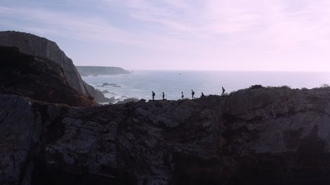 Silhouette of active hiking group on rocky trail with beautiful algarve ocean landscape in background during sunlight.